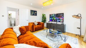Una sala moderna con un amplio sofá modular naranja, una mesa de centro de vidrio y un televisor de pantalla plana montado en la pared.