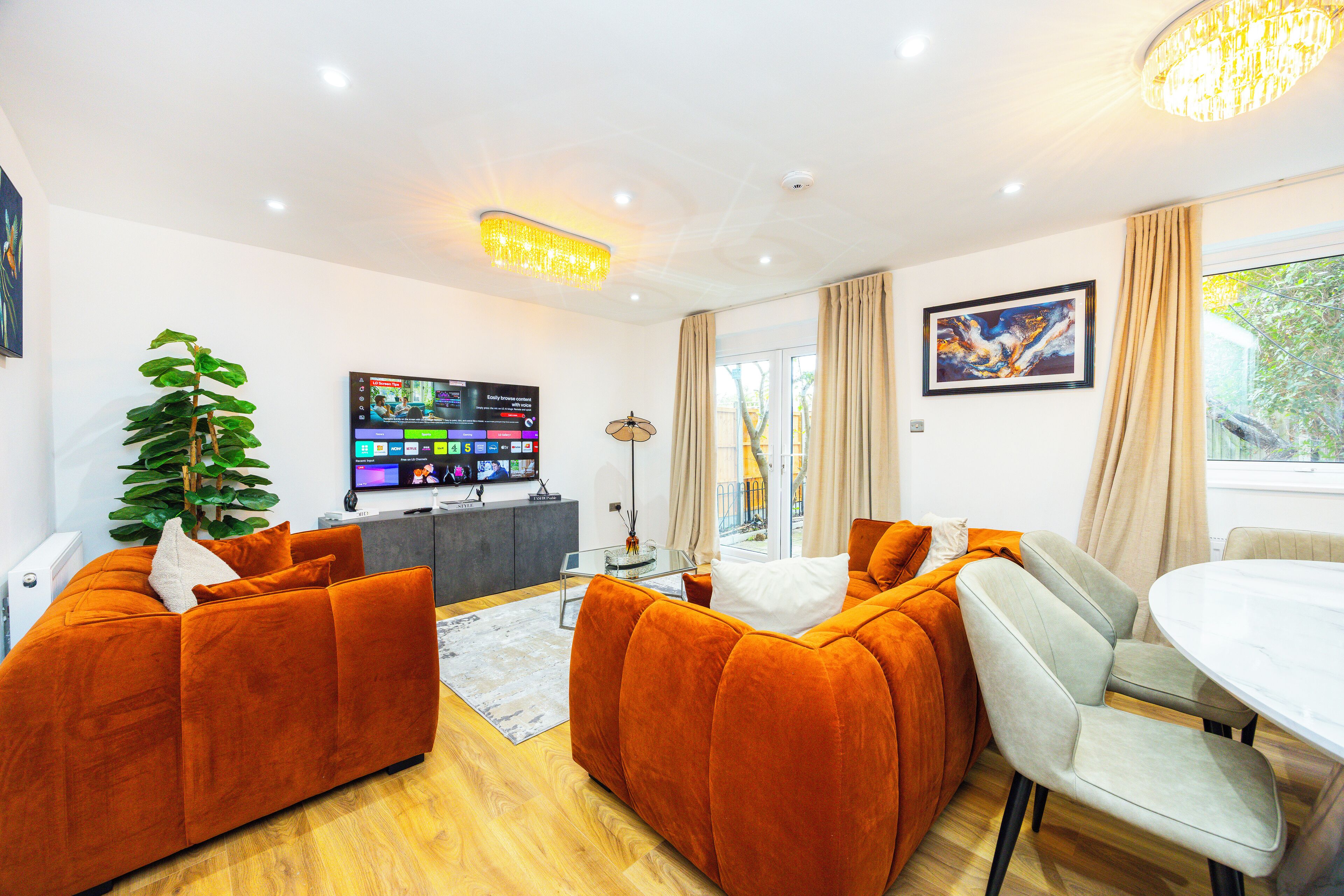 Een moderne woonkamer met oranje banken, een flatscreentelevisie en een eethoek met een tafel en stoelen.