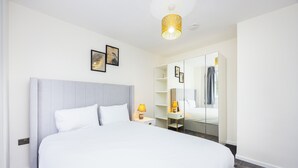 Una habitación de hotel moderna con una cama grande, una mesita de noche con lámpara, un armario y un espejo.