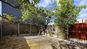 Un patio trasero con cerco de madera, un árbol y un patio empedrado.