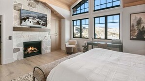 A spacious bedroom with a stone fireplace, a large bed, and a view of the mountains through large windows. - Stag Lodge at Deer Valley Resort - Four Bedroom with Spa #30 4 Condo (Park City)
