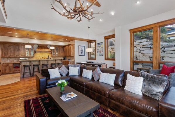 A spacious living area with a brown leather sofa, a wooden coffee table, and a kitchen in the background.