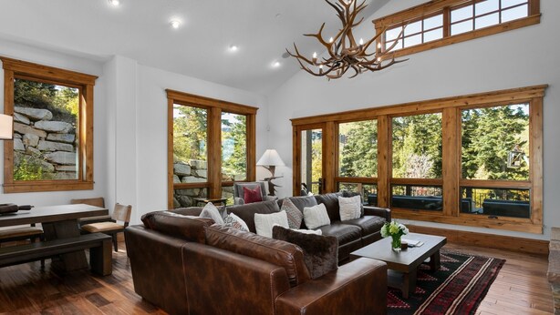 A spacious living room with a leather sofa, wooden dining table, and large windows offering a view of trees. - Lookout at Deer Valley Resort - Four Bedroom Residence with Spa #6559 4 Condo (Park City)