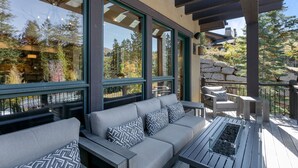 A covered outdoor seating area with a sofa and chairs, large windows, and a stone wall in the background. - Lookout at Deer Valley Resort - Four Bedroom Residence with Spa #6559 4 Condo (Park City)