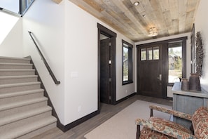 A staircase leading to a dark wooden door, a patterned armchair, and a light-colored carpet.