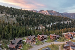 A lodge with multiple wooden cabins, surrounded by dense forest and mountains in the background.