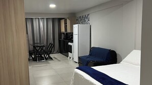 A hotel room with a bed, a desk, a chair, a kitchenette, and a curtain. - Catamarã Pé da Areia (Angra dos Reis)