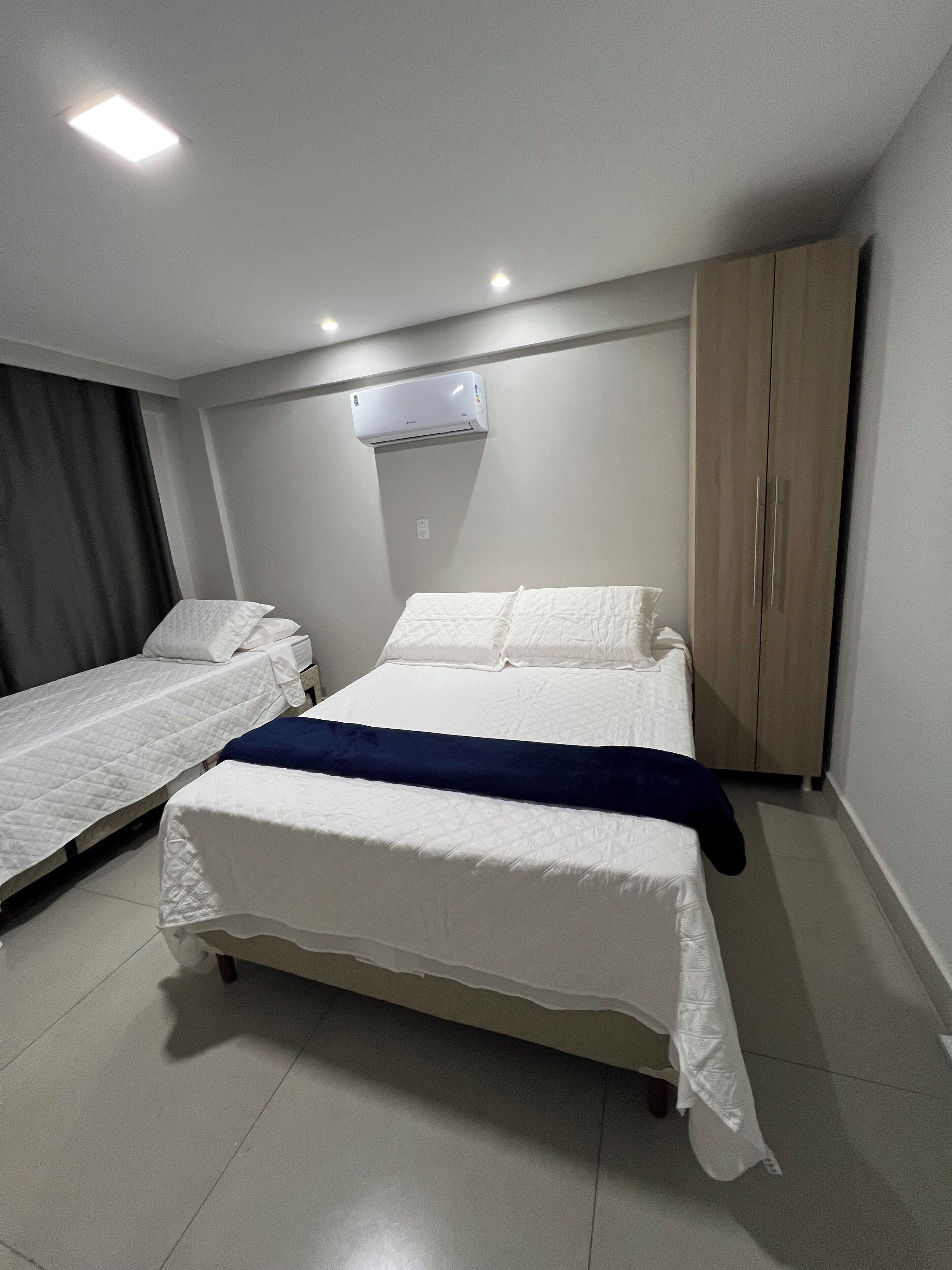 Habitación de hotel con dos camas individuales, una cama más grande, un armario y una lámpara en el techo.