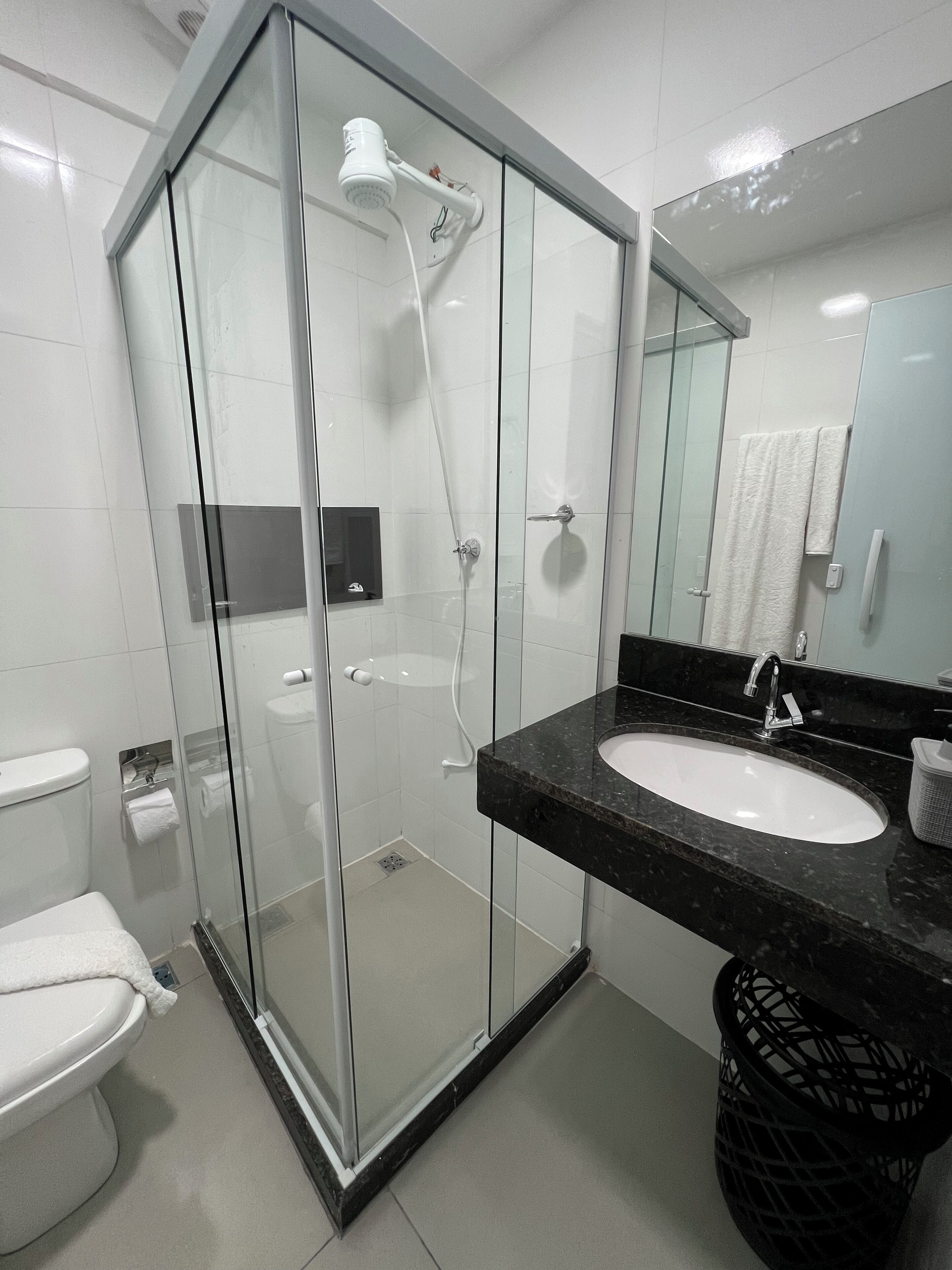 Un bagno moderno con doccia vetrata, lavabo in marmo nero e water bianco.