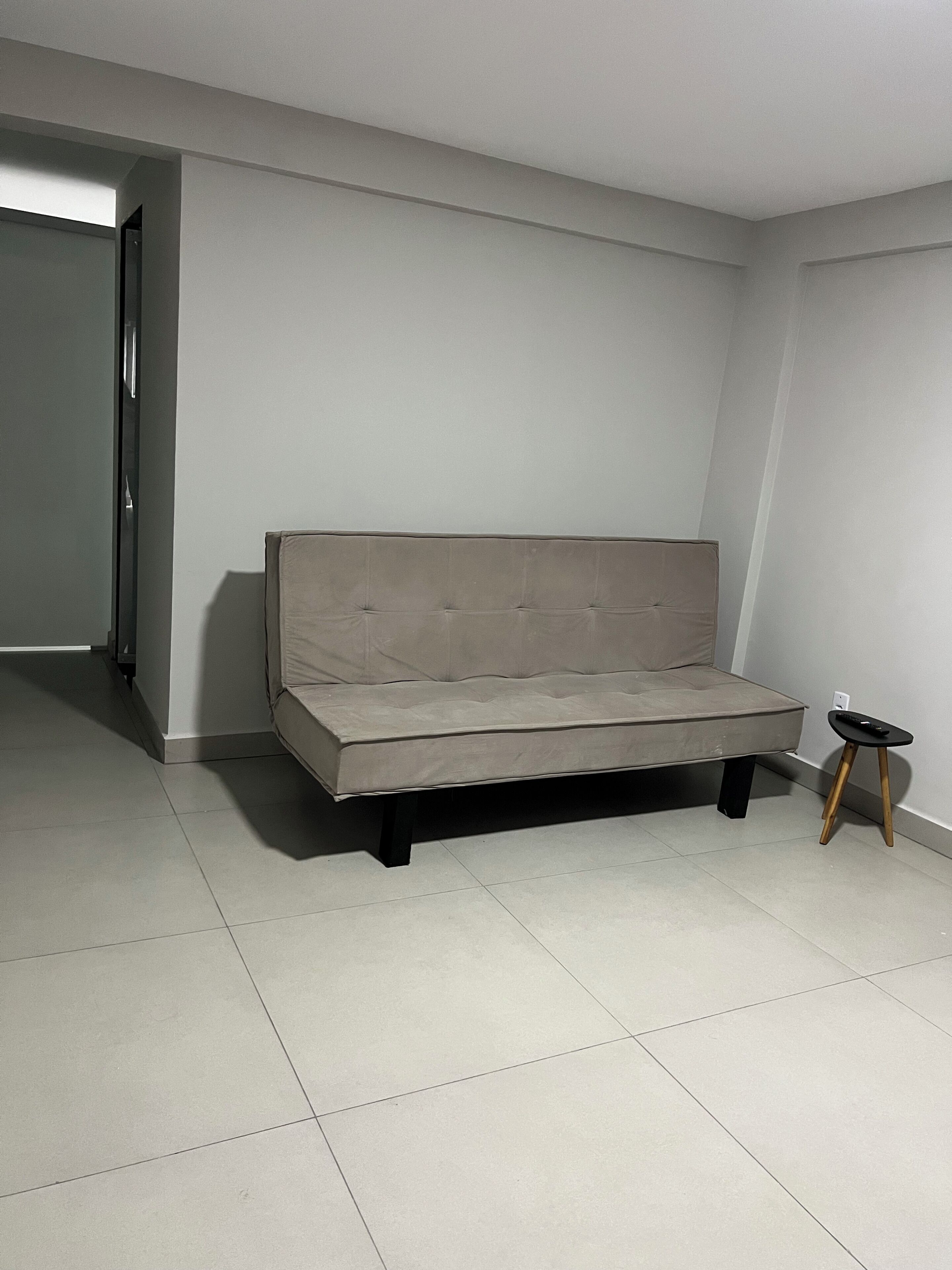 Una sala de estar minimalista con un sofá gris, una mesita auxiliar negra y suelo de baldosas.