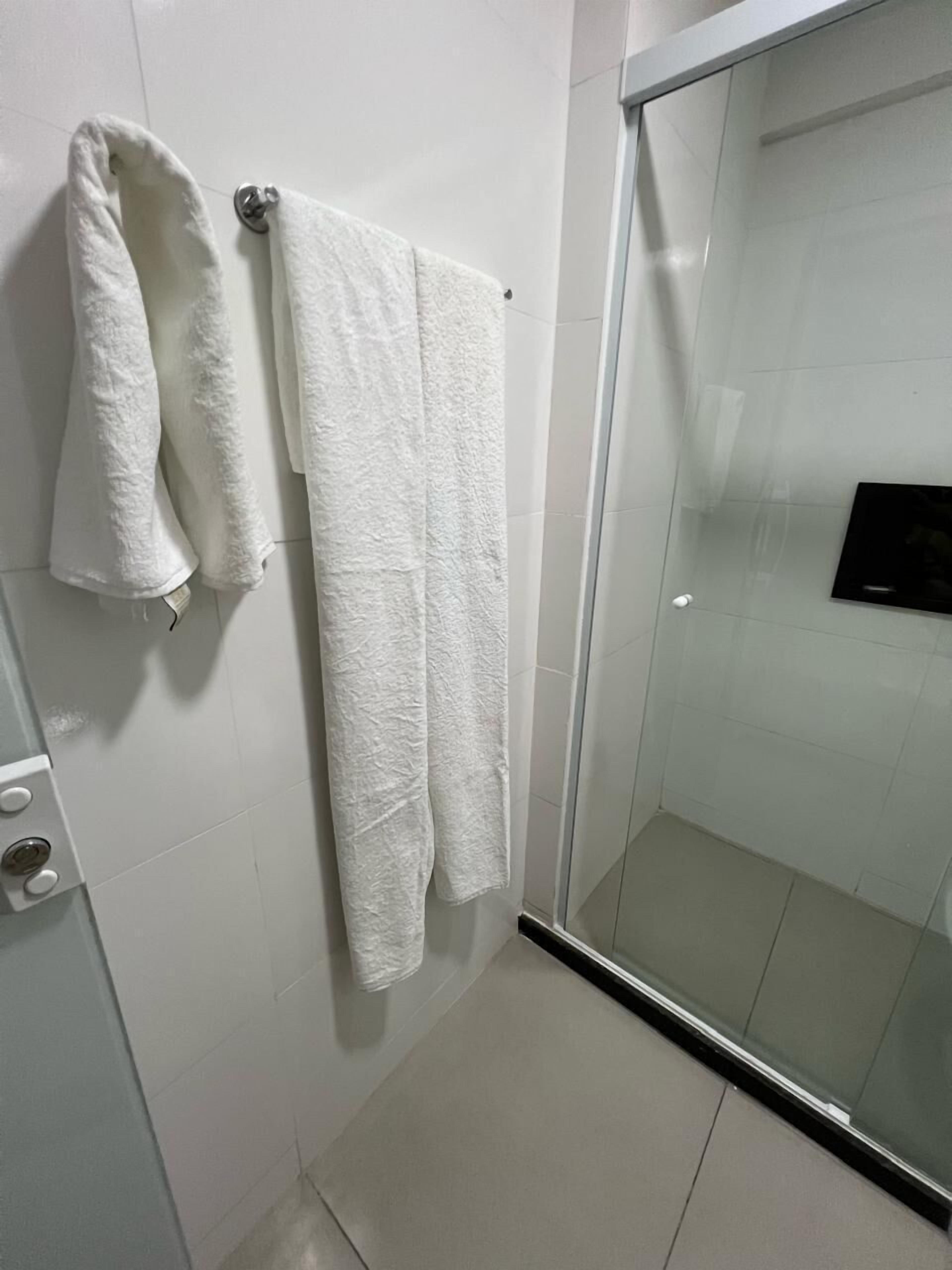 A bathroom with white tiles, a glass shower enclosure, and two white towels hanging on a rack.