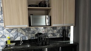 A compact kitchen with wooden cabinets, a microwave, a kettle, and a sink. - Catamarã Pé da Areia (Angra dos Reis)