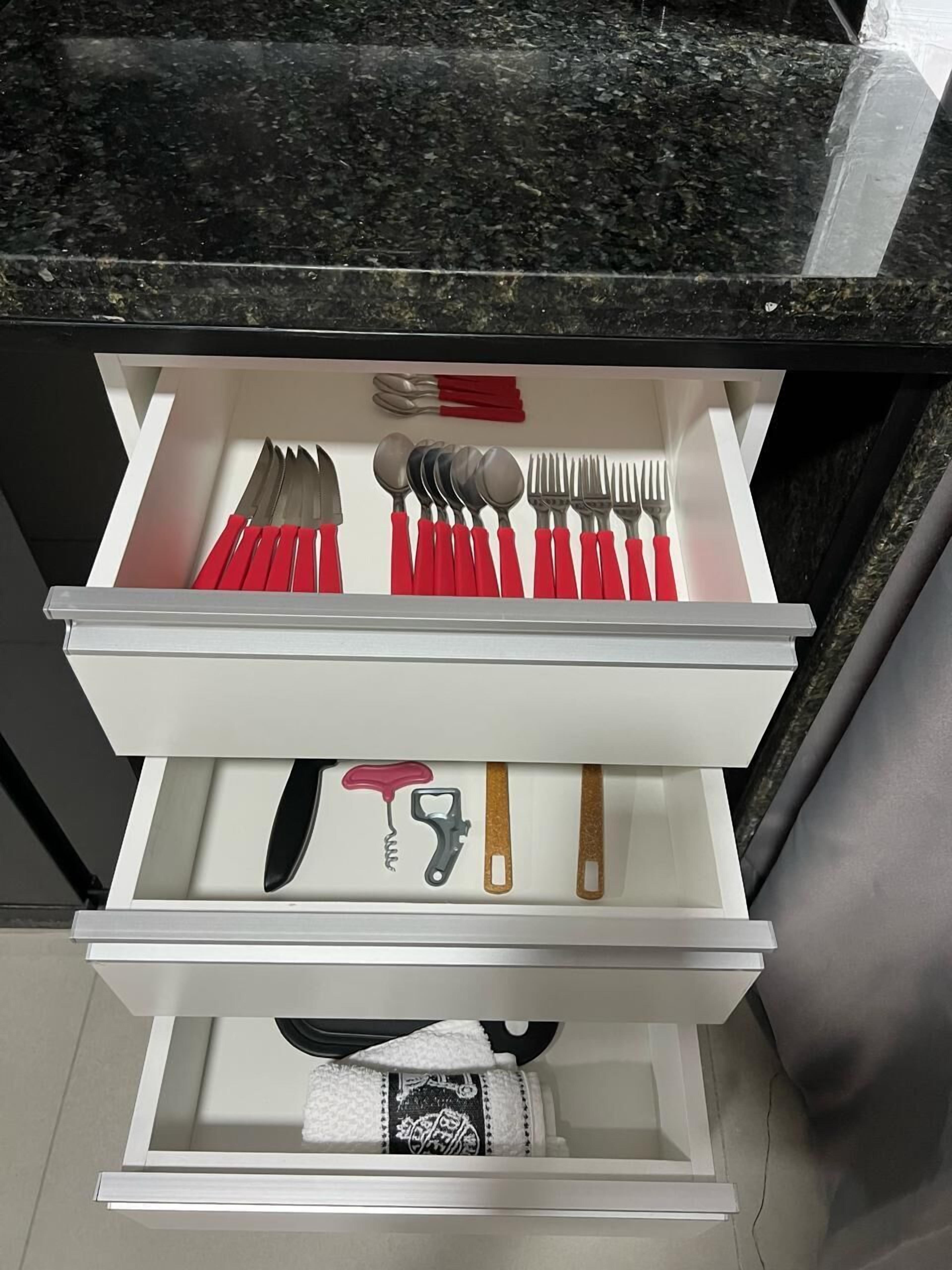 Un cajón con cubiertos y un abrelatas.