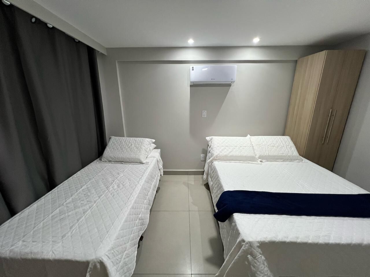Una habitación de hotel con dos camas individuales, un armario, aire acondicionado y suelo de baldosas.
