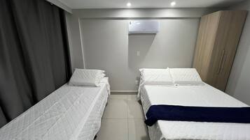 A hotel room with two single beds, a wardrobe, a ceiling-mounted air conditioner, and a curtain on the left side.