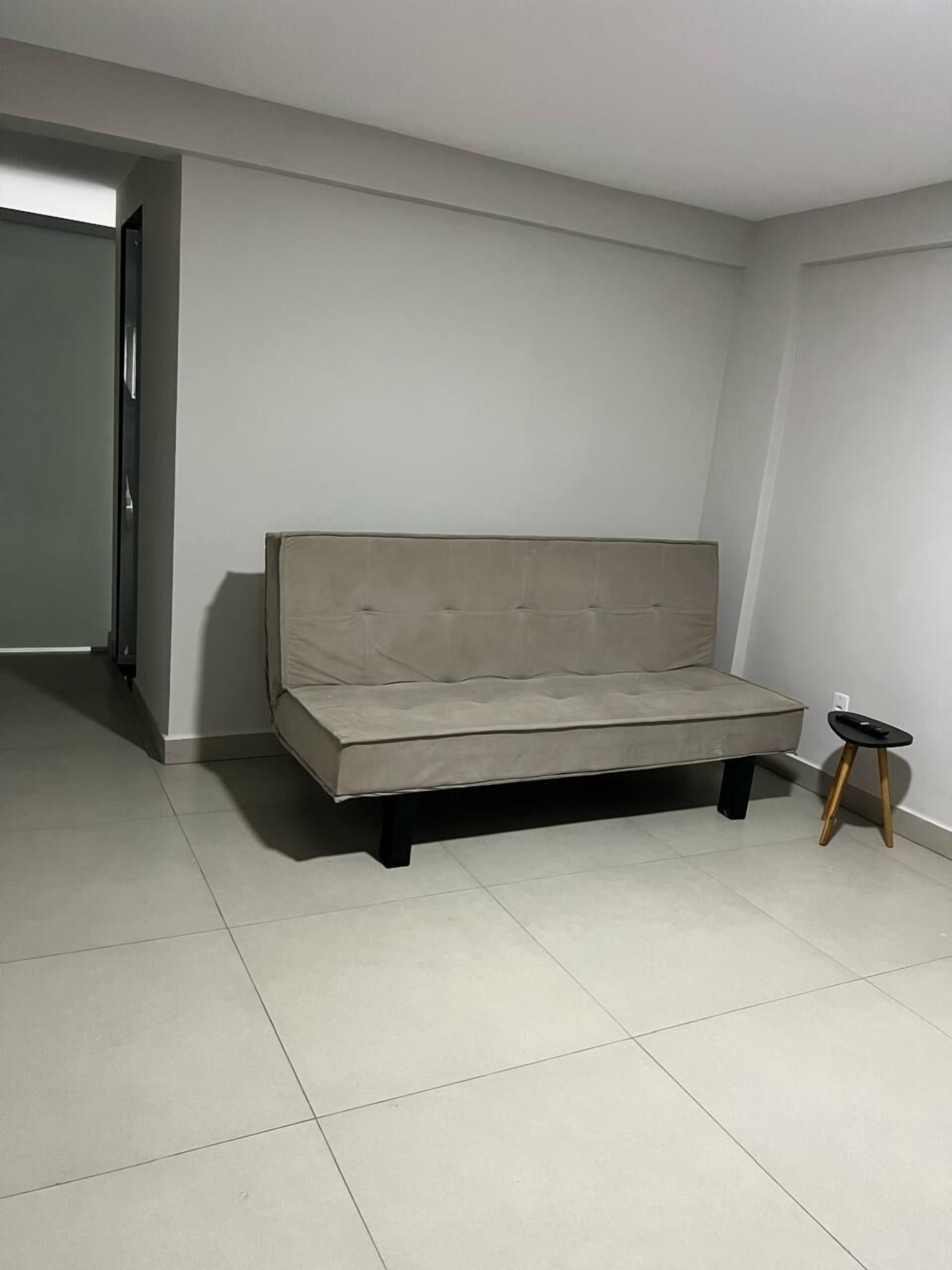 A minimalist living room with a sofa, a small stool, and a tiled floor.