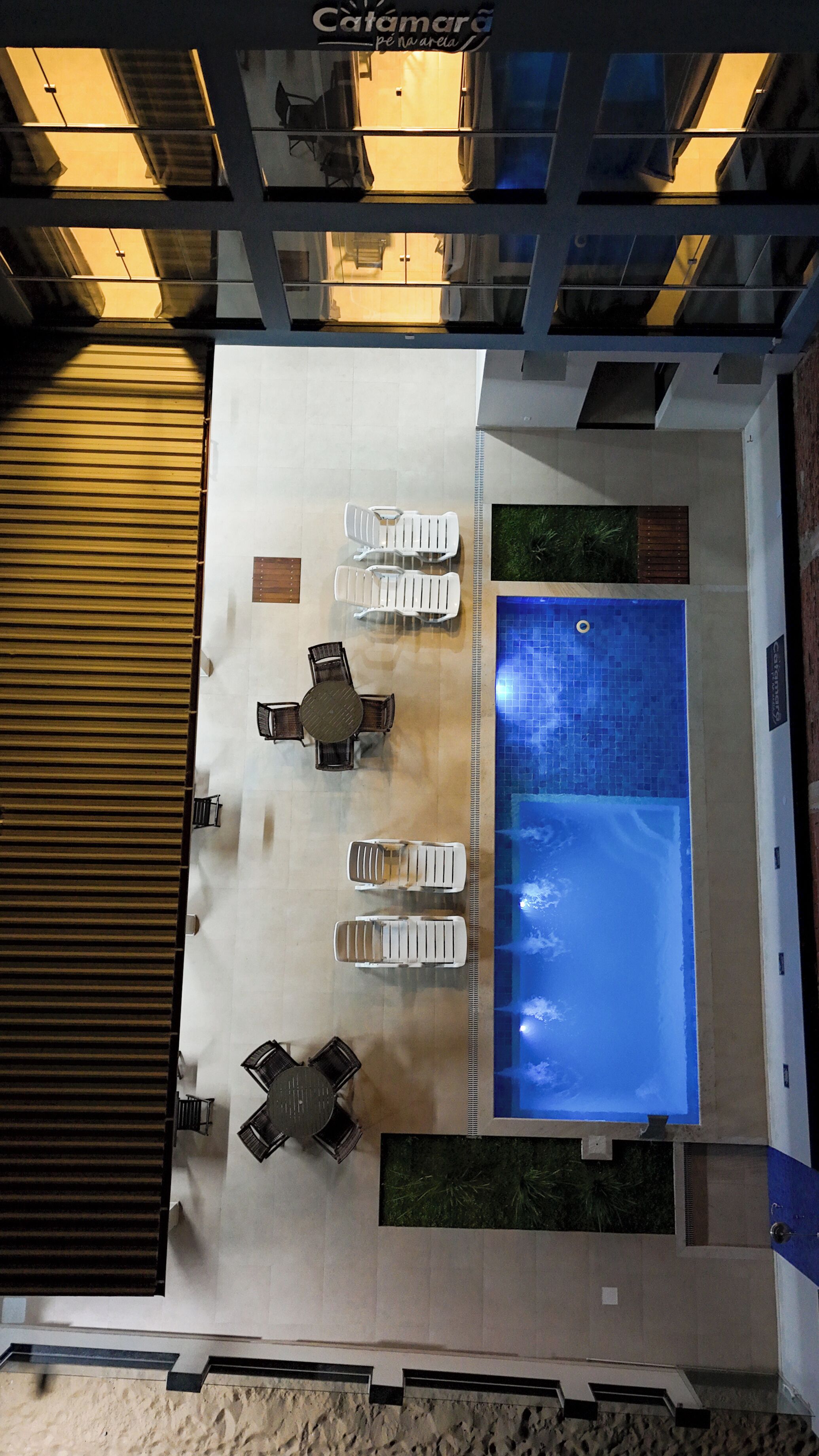 Zona de piscina en la azotea con sillones de descanso y una mesa, rodeada por un techo alto con tragaluces.