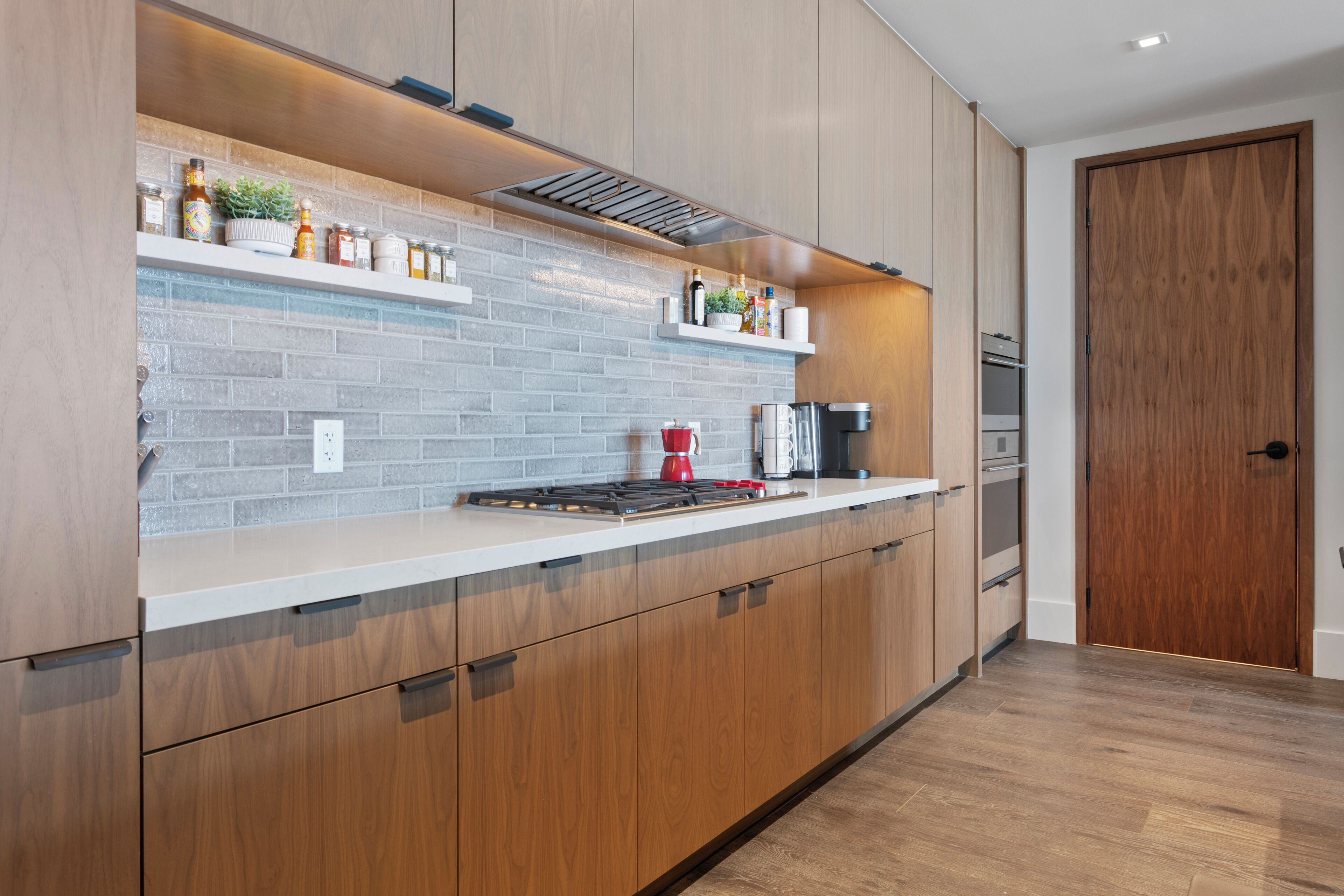 A modern kitchen with wooden cabinets, a brick backsplash, and a stainless steel range hood.