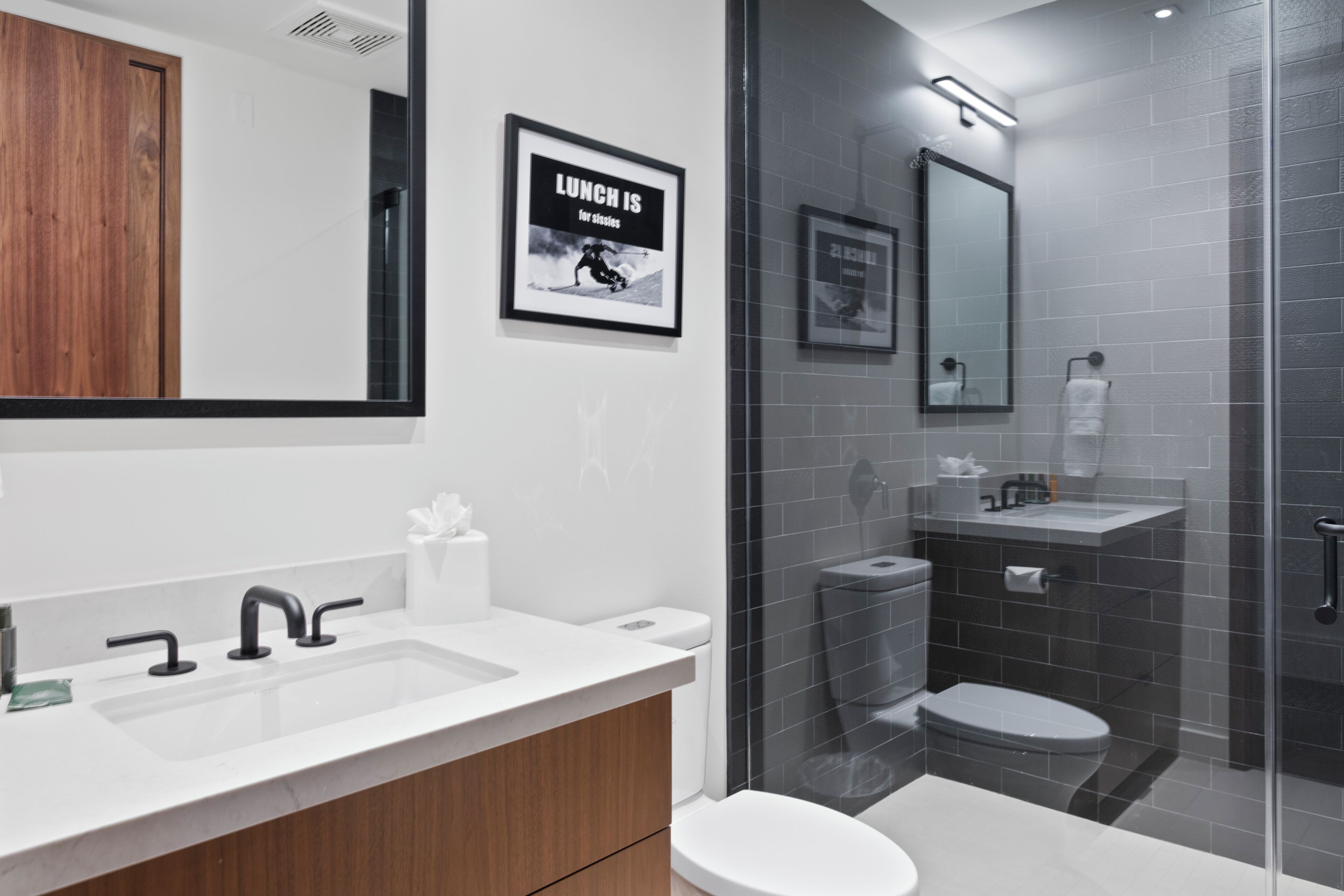 A modern bathroom with a white sink, wooden cabinet, and a glass shower enclosure.