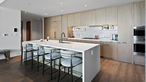 A modern kitchen with a large island, bar stools, wooden cabinets, and stainless steel appliances.