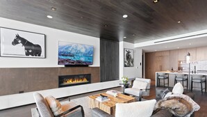 A modern living room with a fireplace, a television mounted on the wall, and a dining area in the background.