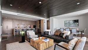 A modern living room with a large sofa, a coffee table, and a dining area with a kitchen in the background.