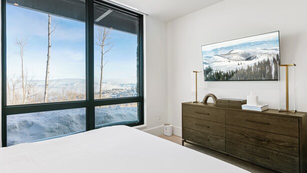 A bedroom with a large window, a bed, a dresser, and a painting of a snowy landscape. - Argent At Deer Valley Resort - Hotel Room #105a Hotel Room (Park City)