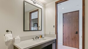 A modern bathroom with a large mirror, a sink, and a wooden door. - Argent At Deer Valley Resort - Hotel Room #105b Hotel Room (Park City)