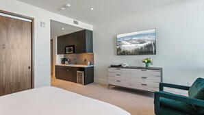 A modern hotel room with a large bed, a green armchair, a dining area with a kitchen, and a large window with a snowy landscape view. - Argent At Deer Valley Resort - Hotel Room #105b Hotel Room (Park City)
