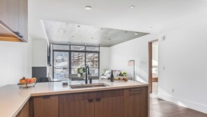 A modern kitchen with a large island, a view of a snowy landscape through large windows, and a wooden floor. - Argent at Deer Valley Resort - Two Bedroom Deluxe #401 2 Condo (Park City)