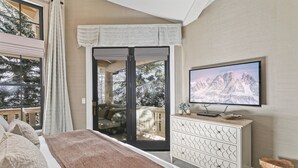 Une chambre à coucher comprenant un lit, une télévision, une commode et un balcon avec vue sur les arbres.