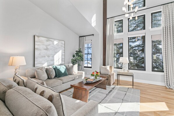 A modern living room with a large window, a sofa set, a coffee table, and a lamp.