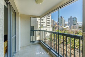 A balcony with a view of a cityscape, including buildings and greenery. - Apto Moderno c/ Churrasq. e Garagem UCR0505 (Porto Alegre)