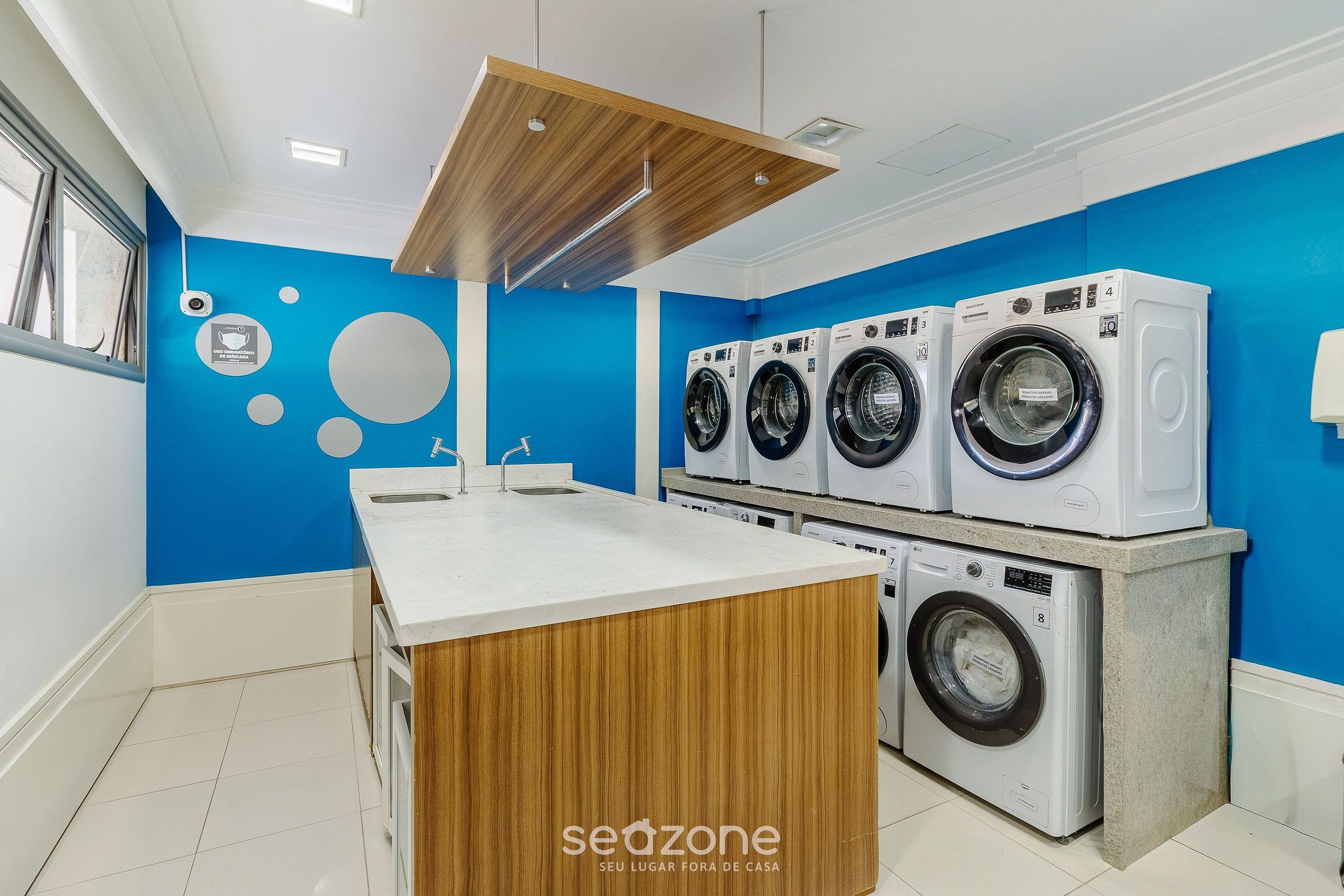 A modern laundry room with four washing machines, a wooden counter, and a blue wall.