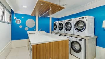 A modern laundry room with four washing machines, a wooden counter, and a blue wall.