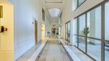 A hotel corridor with a marble floor, large windows, and a modern light fixture.