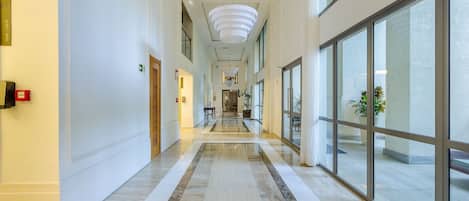 A hotel corridor with a marble floor, large windows, and a modern light fixture.