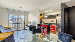A modern apartment with a dining area, kitchen, and large windows offering city views. - Apto Moderno c/ Churrasq. e Garagem UCR0505 (Porto Alegre)