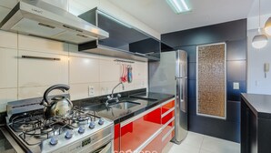 A modern kitchen with stainless steel appliances, a gas stove, and red cabinetry. - Apto Moderno c/ Churrasq. e Garagem UCR0505 (Porto Alegre)