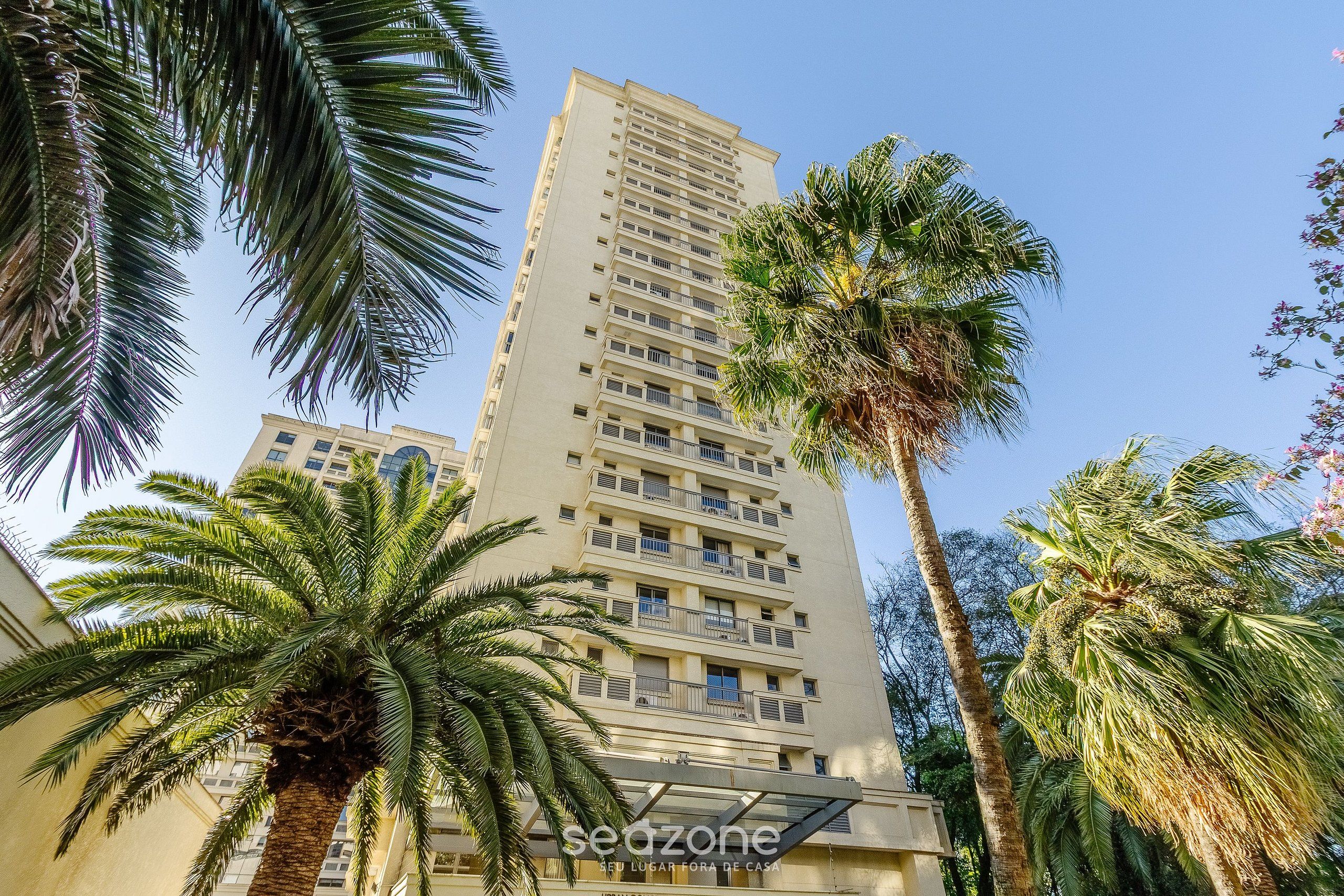 A high-rise building with multiple balconies and palm trees in the foreground.