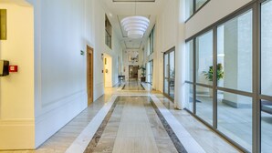 A long, well-lit hallway with marble flooring, large windows, and a modern chandelier. - Apto Moderno c/ Churrasq. e Garagem UCR0505 (Porto Alegre)