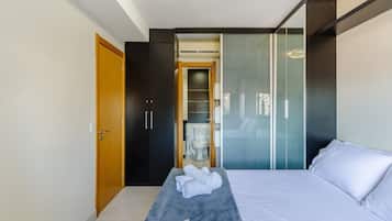 Quarto de hotel moderno com cama, um banco com toalhas, guarda-roupa e divisória de vidro.