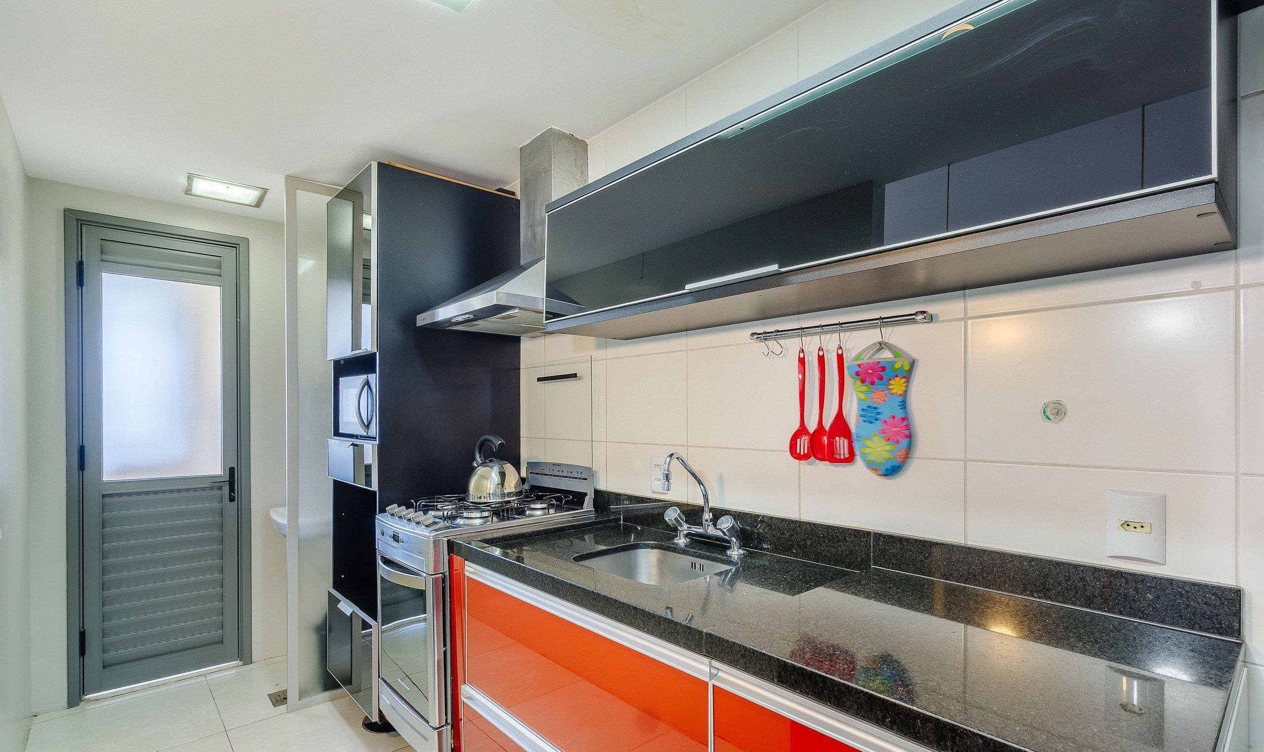 Cozinha moderna com eletrodomésticos de aço inoxidável, bancada preta e painel de cozinha colorido.