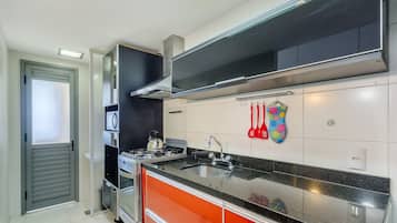 Cozinha moderna com eletrodomésticos de aço inoxidável, bancada preta e painel de cozinha colorido.