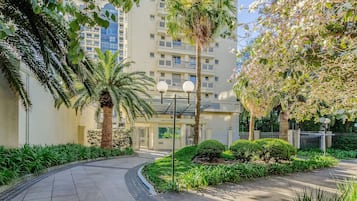 A residential building with a paved walkway, palm trees, and well-maintained greenery.