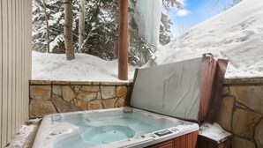 A hot tub with stone walls and a view of snow-covered trees.