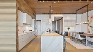 A modern kitchen with a central island, white cabinetry, and a wooden ceiling.