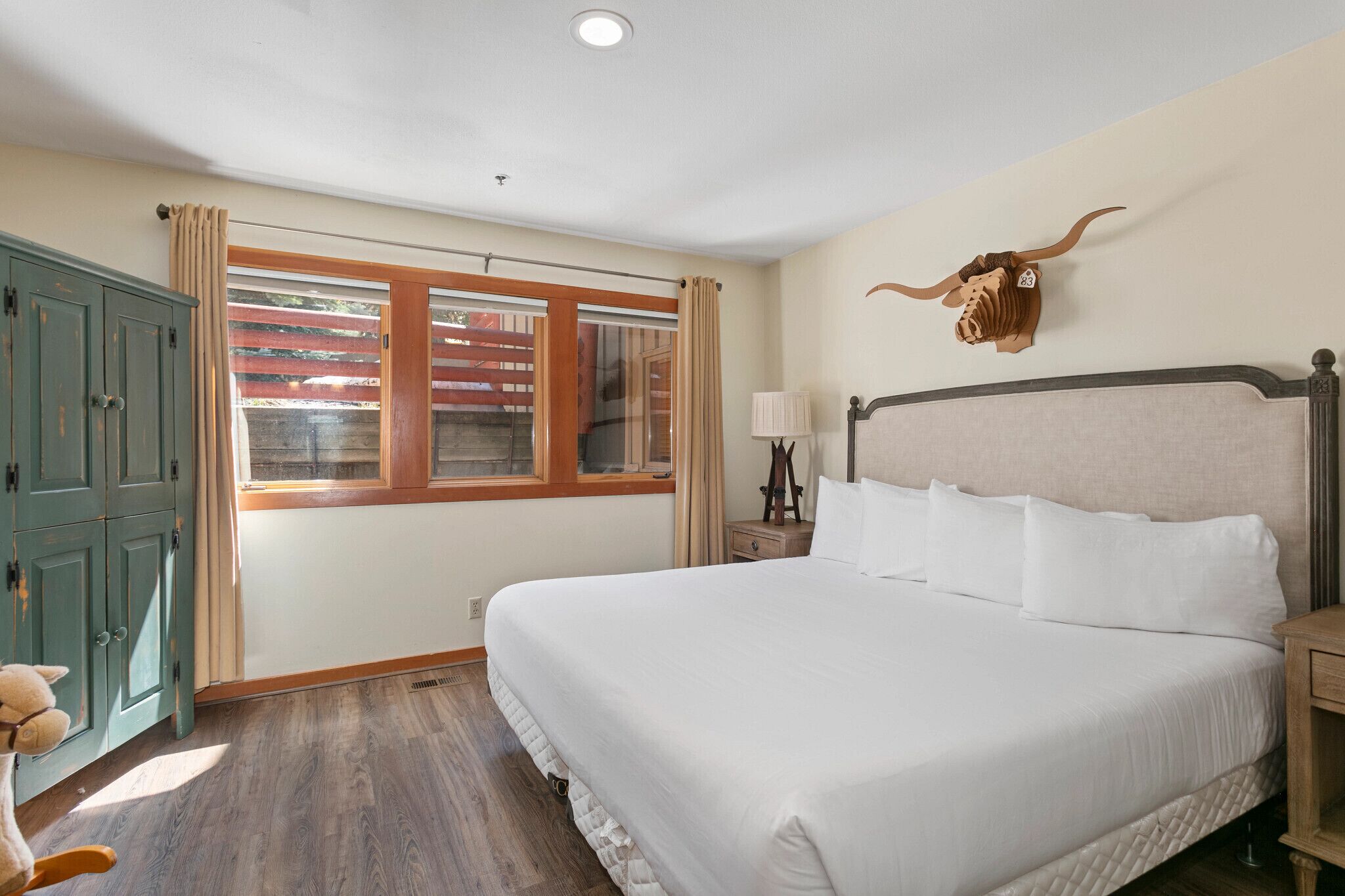 Un dormitorio con una cama grande, cabecero de madera, decoración con cráneo de toro, ventana con cortinas y un armario verde.