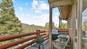 Una terraza de madera con una parrilla y sillas, con vistas a un paisaje montañoso.