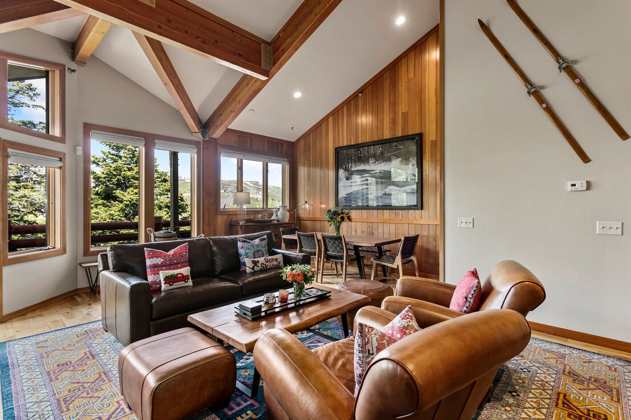 A spacious living room with a large window, a wooden ceiling, and a painting on the wall.